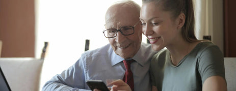 A lovely image of an elderly man and his daughter browsing Dementia Black Friday deals on their phone.