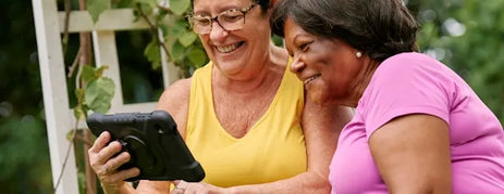 two senior women looking at dementia apps on a tablet and smiling