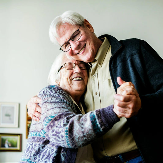 A happy older couple smiling and dancing together at home, enjoying music from a dementia radio.