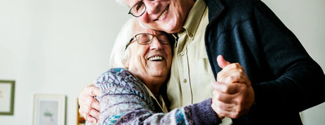 A happy older couple smiling and dancing together at home, enjoying music from a dementia radio.