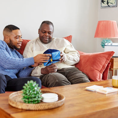Two men sitting on a sofa together, demonstrating the comfort and engagement provided by holding a blue fabric sensory dementia toy.