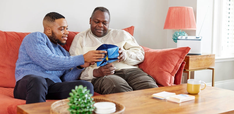 Two men sitting on a sofa together, demonstrating the comfort and engagement provided by holding a blue fabric sensory dementia toy.
