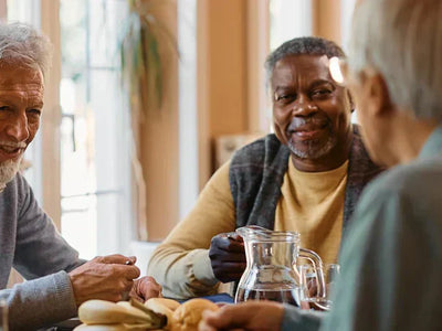 A group of elderly came home residents take part in a group activity. They are smiling and sat around a table with refreshments.