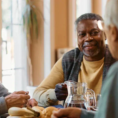A group of elderly came home residents take part in a group activity. They are smiling and sat around a table with refreshments.