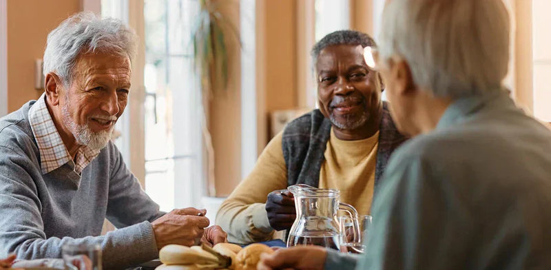 A group of elderly came home residents take part in a group activity. They are smiling and sat around a table with refreshments.