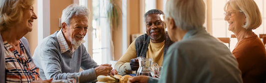 A group of elderly came home residents take part in a group activity. They are smiling and sat around a table with refreshments.