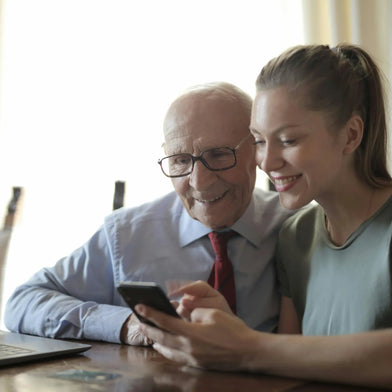 A lovely image of an elderly man and his daughter browsing Dementia Black Friday deals on their phone.