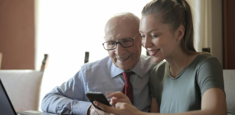 A lovely image of an elderly man and his daughter browsing Dementia Black Friday deals on their phone.