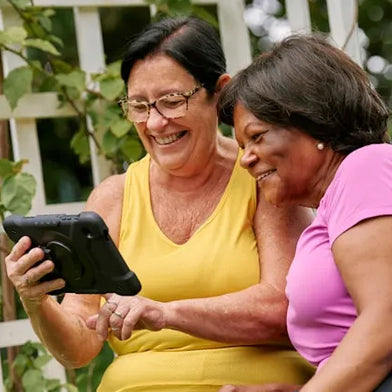 two senior women looking at dementia apps on a tablet and smiling