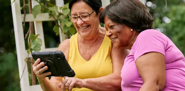 two senior women looking at dementia apps on a tablet and smiling