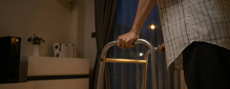 An elderly person gripping a walker in a dark room, illustrating nighttime dementia wandering