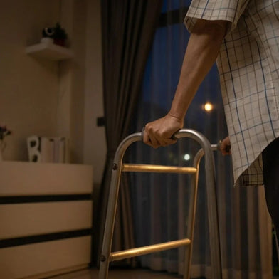 An elderly person gripping a walker in a dark room, illustrating nighttime dementia wandering