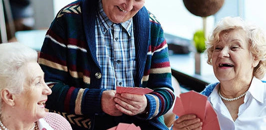 Three older friends enjoying a card game together, a sociable summer activity for people with dementia