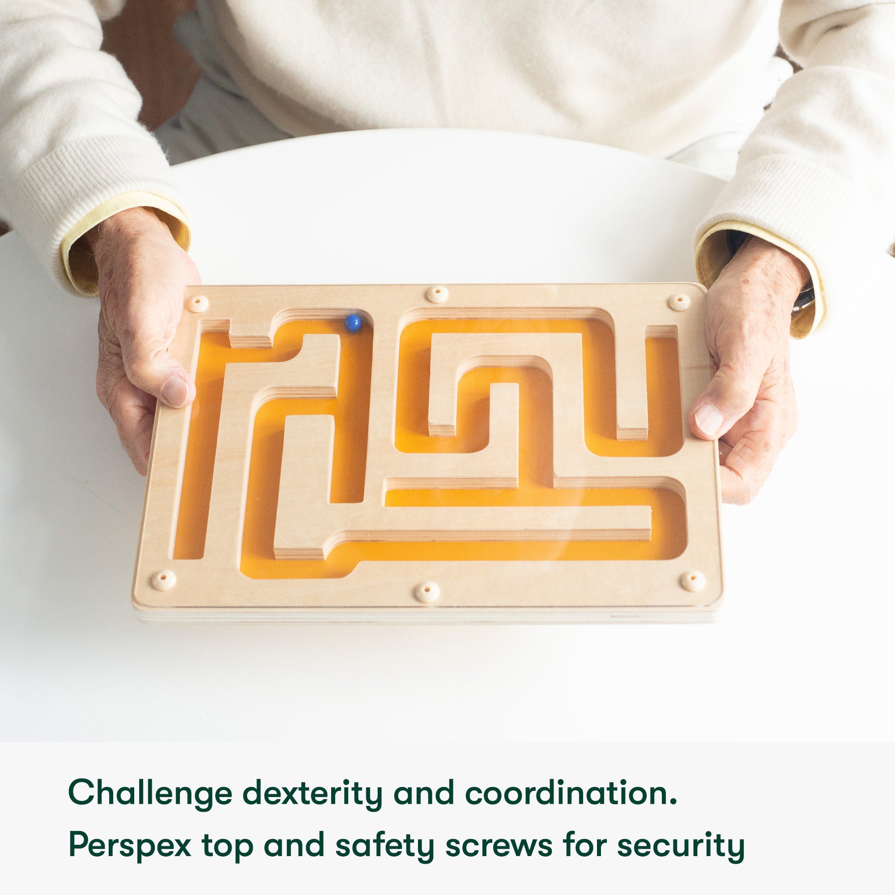 Elderly hands hold a wooden maze, a dementia activity promoting dexterity and coordination, ideal for care home residents.