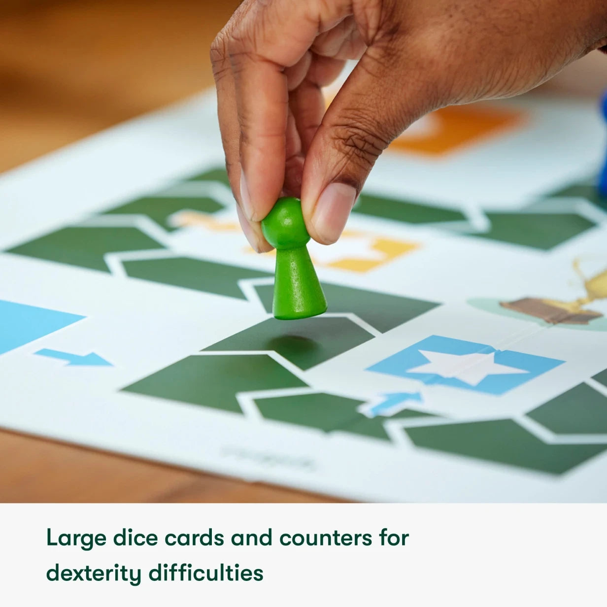 A hand places a large green game piece on a board designed for dementia-friendly play.
